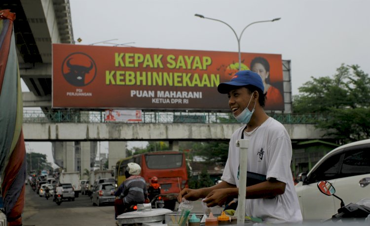 Penjual cilok tengah melayani pembeli di Jalan Jenderal Sudirman, dengan latar belakang baliho besar Kepak Sayap Kebhinnekaan milik Ketua DPR RI, Puan Maharani, Rabu (25/8). (humaidy kenedy/rmolsumsel.id)