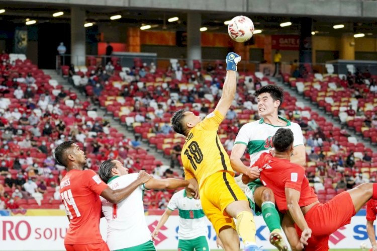 Kiper Singapura Hassan Sunny meninju bola untuk mengamankan dari tandukan bek Indonesia Elkan Baggott pada laga di National Stadium, Rabu malam (22/12). (AFF Suzuki Cup 2020/rmolsumsel.id)