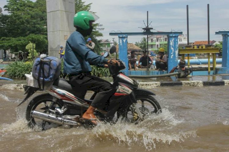 Pengendara menembus banjir di Simpang Polda dengan latar belakang petugas Dinas PUPR Palembang yang kewalahan dan beristirahat/Foto: RMOL
