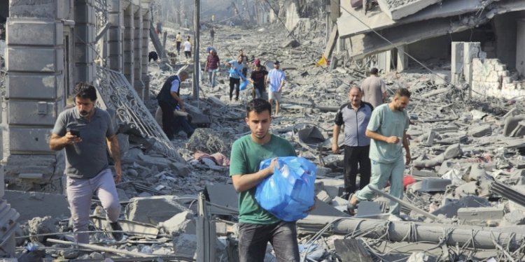 Warga Palestina berjalan melewati puing-puing bangunan yang hancur akibat serangan udara Israel di Kota Gaza pada Rabu, 11 Oktober 2023/AP