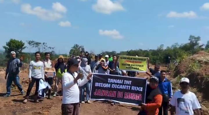Warga Desa Keban Agung membentangkan spanduk 'Tanah ini belum diganti rugi jangan digusur' sebagai bentuk protes mereka. (noviansyah/rmolsumsel.id)