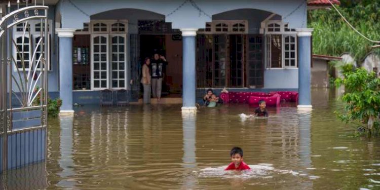 Anak-anak berjalan melewati banjir di luar rumah mereka di Tumpat, pinggiran Kota Bahru, Malaysia, Selasa, 3 Desember 2024/Net